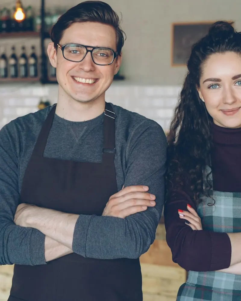 Two café owners in aprons standing behind their counter.