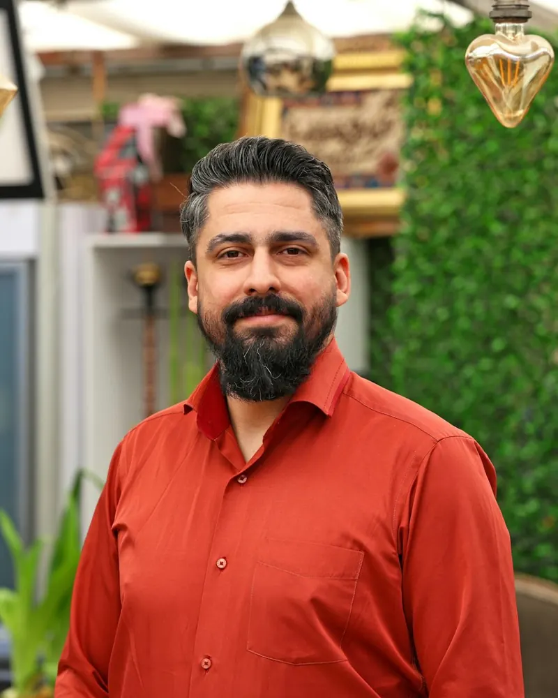A shop owner in a red shirt smiling in his store.