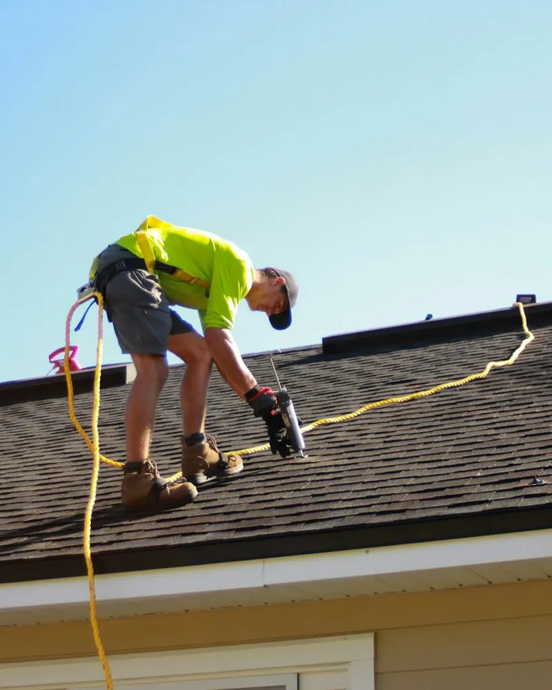 A roofer fastening shingles on a house roof.